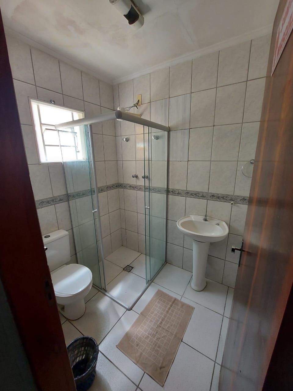 Et badeværelse med brusekabine i glas, toilet, vask og et vindue.