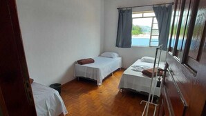 A room with three beds, wooden flooring, a ceiling fan, and a window with curtains. - Novo Hotel (Itajuba)