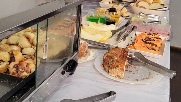 A buffet table with various food items and utensils. - Novo Hotel (Itajuba)