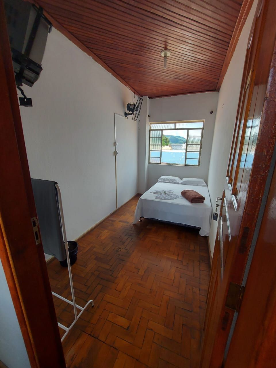 Quarto com uma cama, janela e piso de madeira.