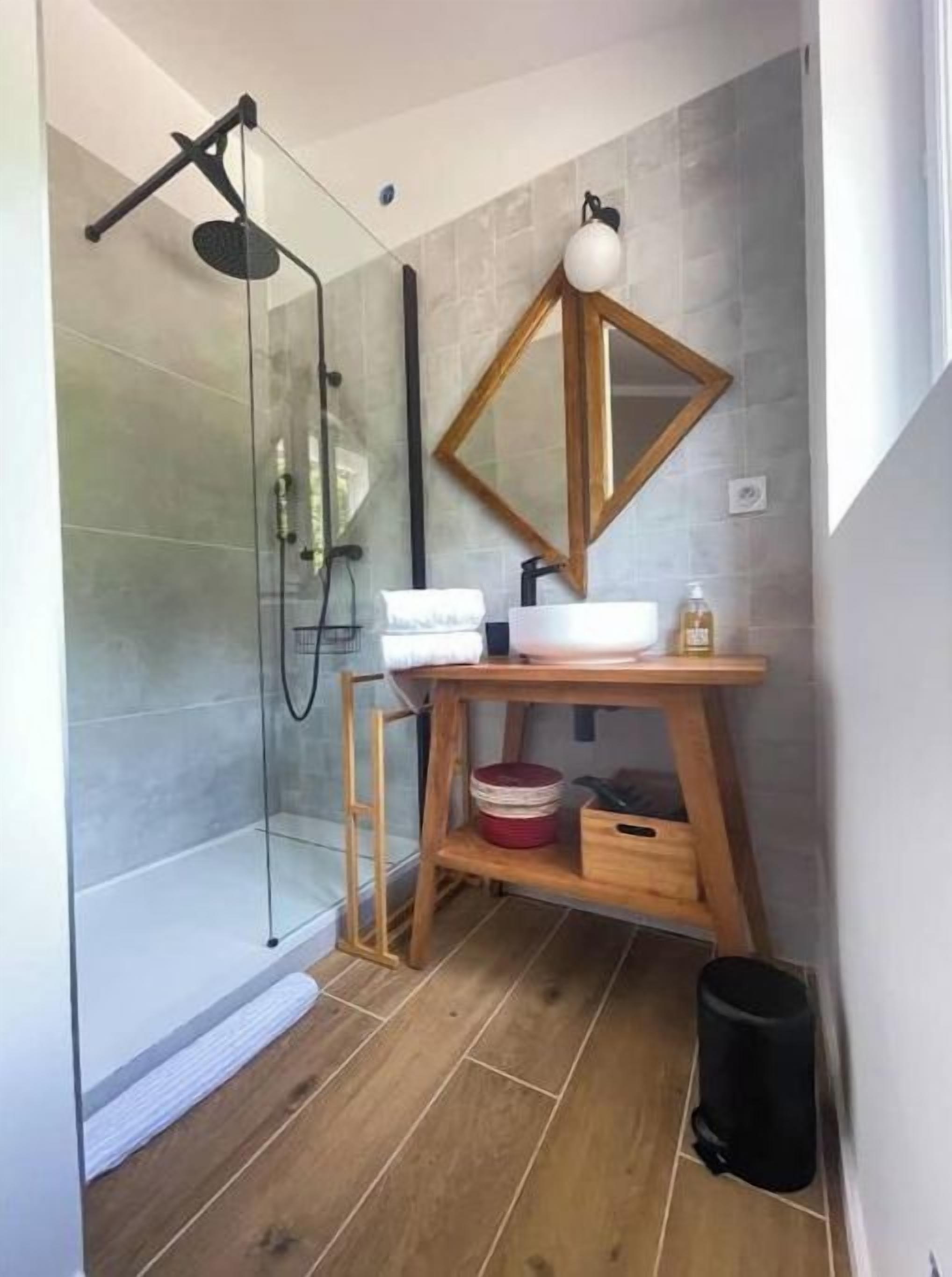 A modern bathroom with a glass shower enclosure, a wooden vanity, and a mirror with a geometric frame.