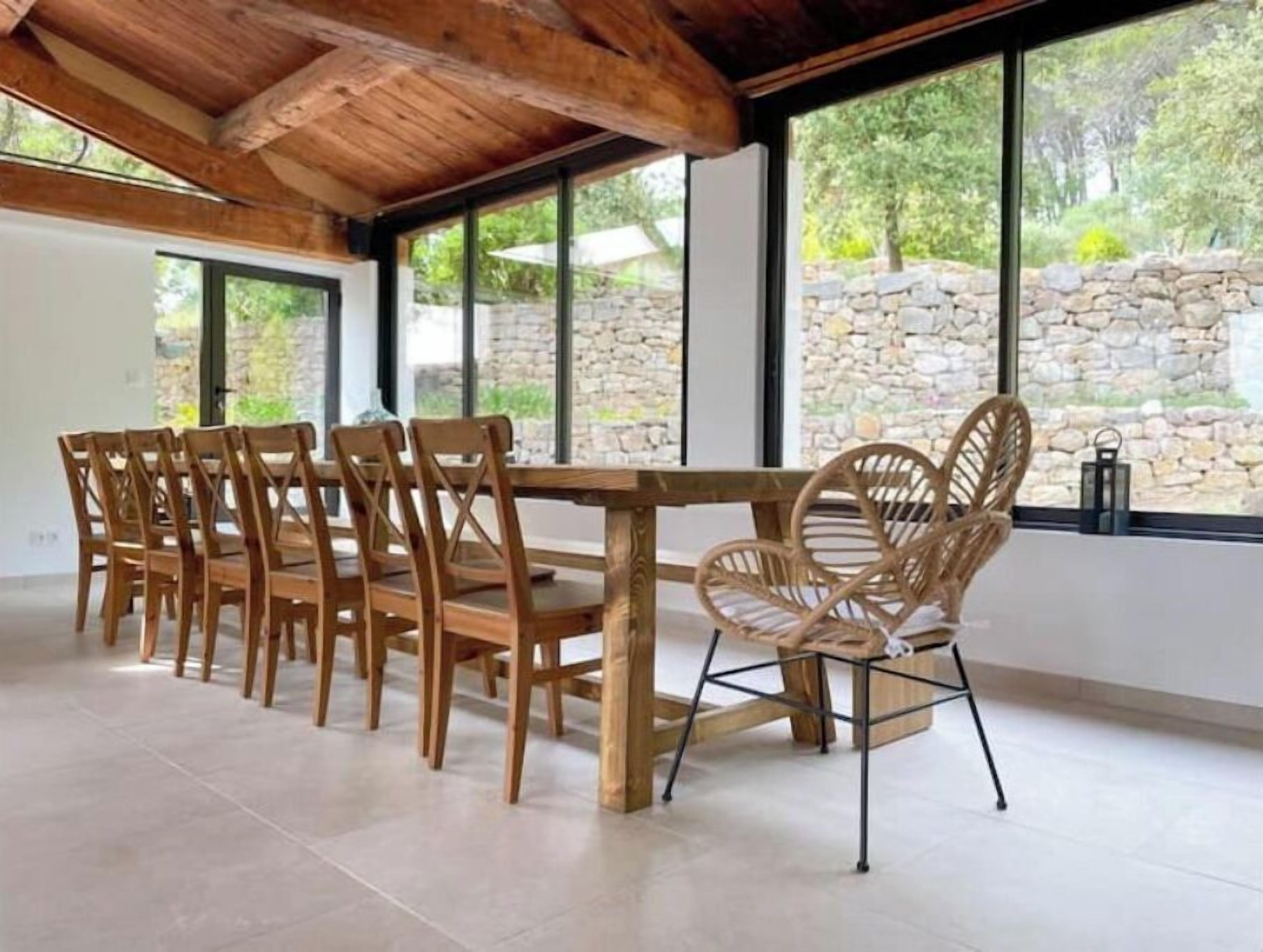 Un comedor con una mesa y sillas de madera, ventanas amplias con vistas a una pared de piedra y techo de madera.