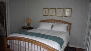 Une chambre à coucher avec un lit en bois, une literie blanche, une petite table de chevet avec une lampe, et quatre tableaux encadrés accrochés au mur.