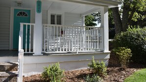 Un porche blanc avec une porte de couleur turquoise, des rampes blanches et un petit jardin agrémenté de paillis et de plantes.
