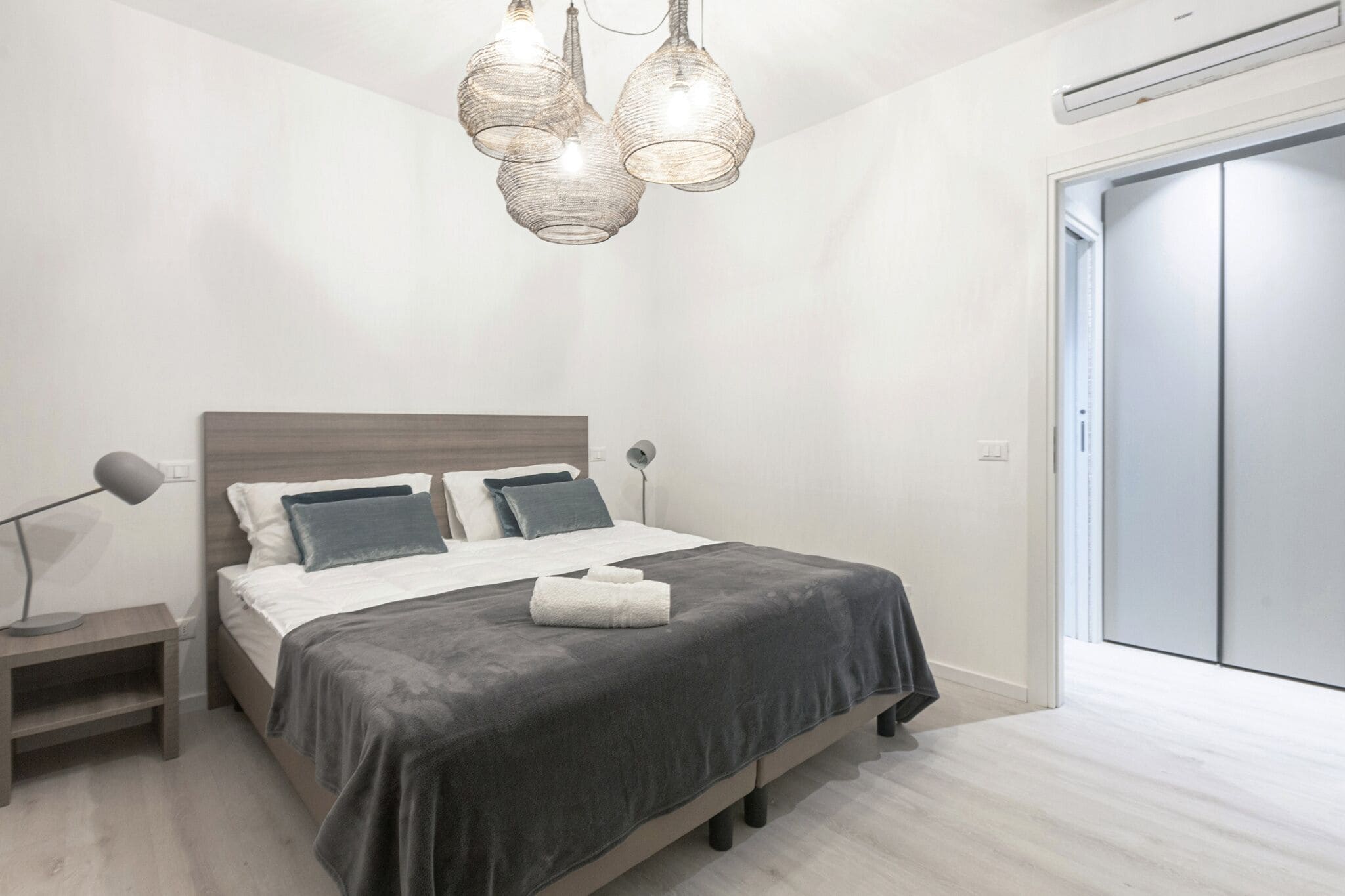 Un dormitorio moderno con cama, mesitas de noche, lámpara y armario.