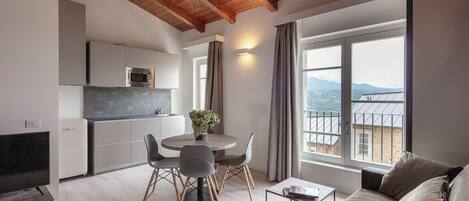 Una cocina moderna con microondas integrado, una zona de comedor con una mesa redonda y sillas, y un sofá con vistas a las montañas.