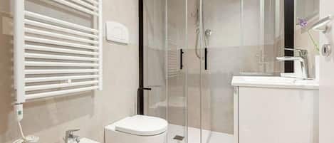 A modern bathroom with a glass-enclosed shower, a white sink, and a toilet.