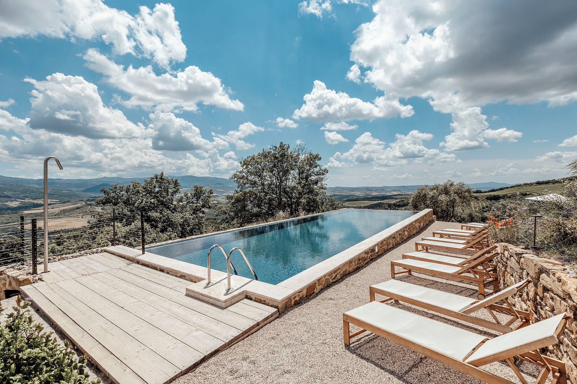 Una piscina infinita con borde de piedra, terraza de madera y sillones de descanso.