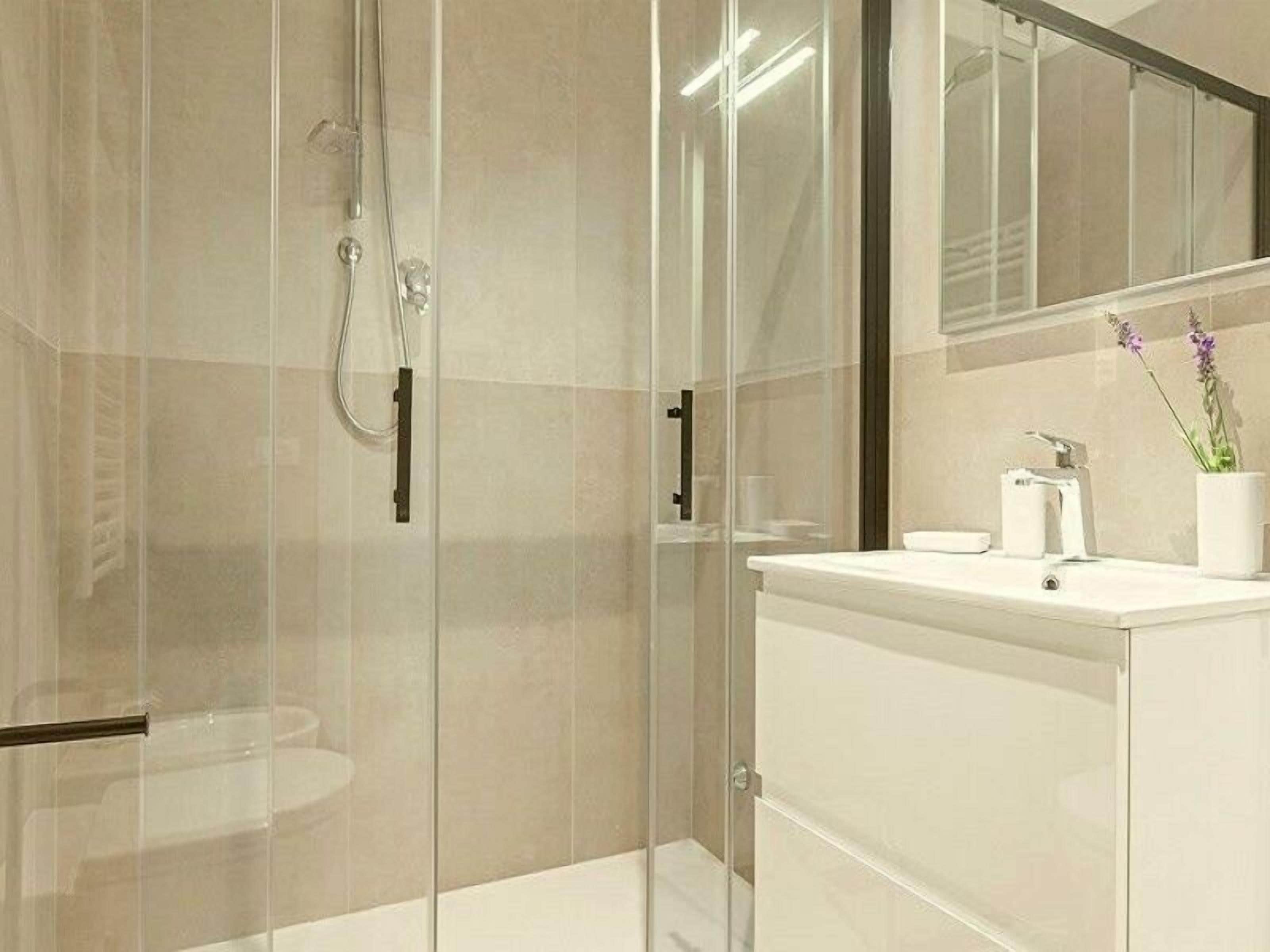 Un baño moderno con ducha de vidrio, un lavamanos blanco y un espejo encima.