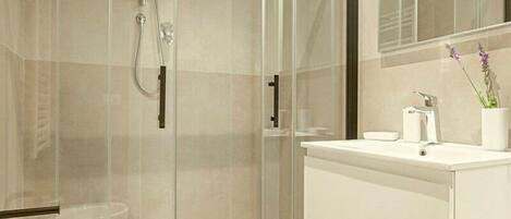 A modern bathroom with a glass-enclosed shower, a white sink, and a mirror above it.