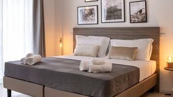 A neatly made bed with a grey bedspread and white pillows, a wooden headboard, and four framed pictures on the wall.