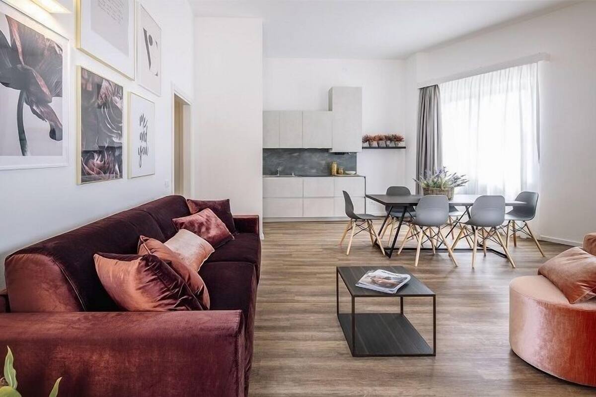 A modern living room with a dark red sofa, a coffee table, and a dining area with a table and chairs.