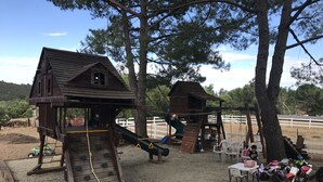 A playground with wooden climbing structures and slides, surrounded by trees and a fenced area. - Ranch in equestrian community (Murrieta)