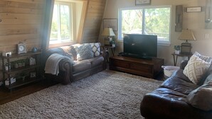 A cozy living room with a fireplace, wooden walls, a large window, and a television. - Ranch in equestrian community (Murrieta)