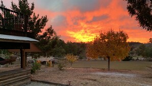 A patio area with a fire pit, a covered seating area, and a view of a sunset over a grassy field. - Ranch in equestrian community (Murrieta)