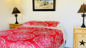 Ein Schlafzimmer mit Holzboden, einem Bett mit rot-weiß gestreifter Bettwäsche, zwei Nachttischen mit Lampen und einem gerahmten Bild an der Wand.
