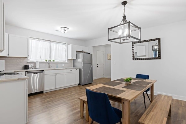 Une cuisine moderne avec des meubles blancs, des appareils en acier inoxydable et une table à manger en bois, assortie de chaises bleues.