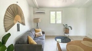 Ein modernes Wohnzimmer mit grauem Sofa, einem Holzesstisch mit Stühlen, einem Wandventilator und einer hängenden Deckenleuchte.