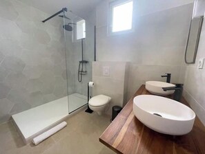 Et moderne badeværelse med en glasbrusekabine, toilet og en trævaskepude med en stor, hvid vask.