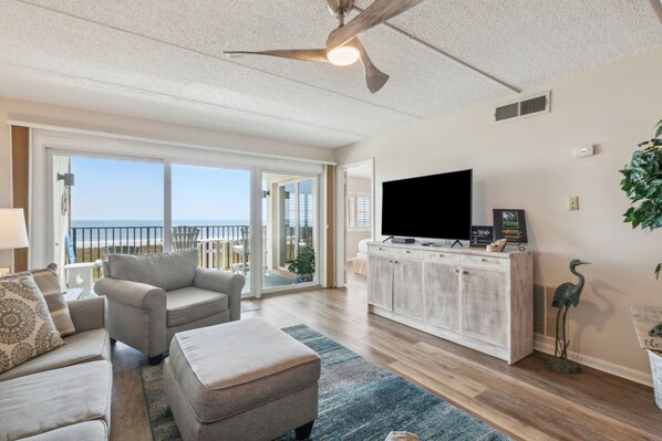 A spacious living room with a large TV, comfortable seating, and a view of the ocean.
