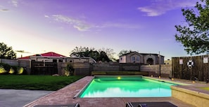 A swimming pool with a wooden deck, a red-roofed building, and a house with a grey facade.