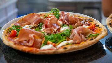 Pizza mit Schinken und Grünzeug auf einem schwarzen Tisch.