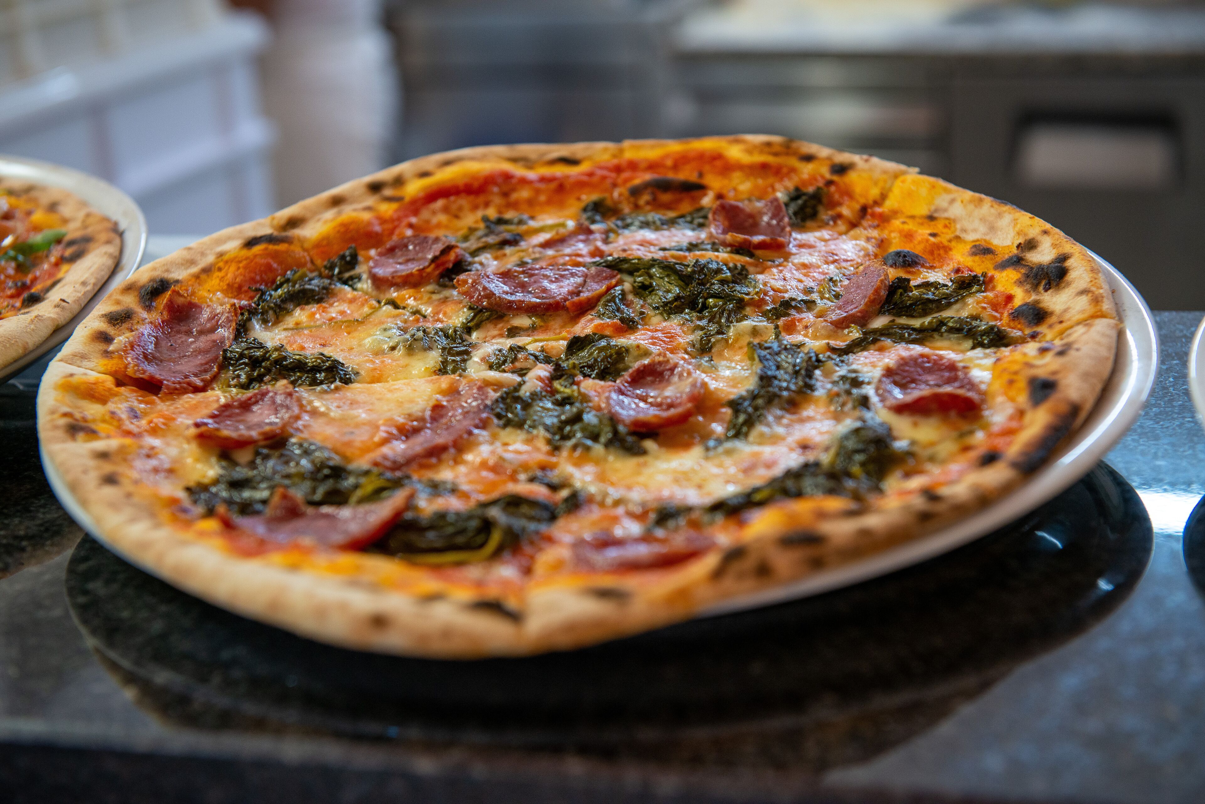 A pizza with visible toppings of pepperoni and greens on a black countertop.