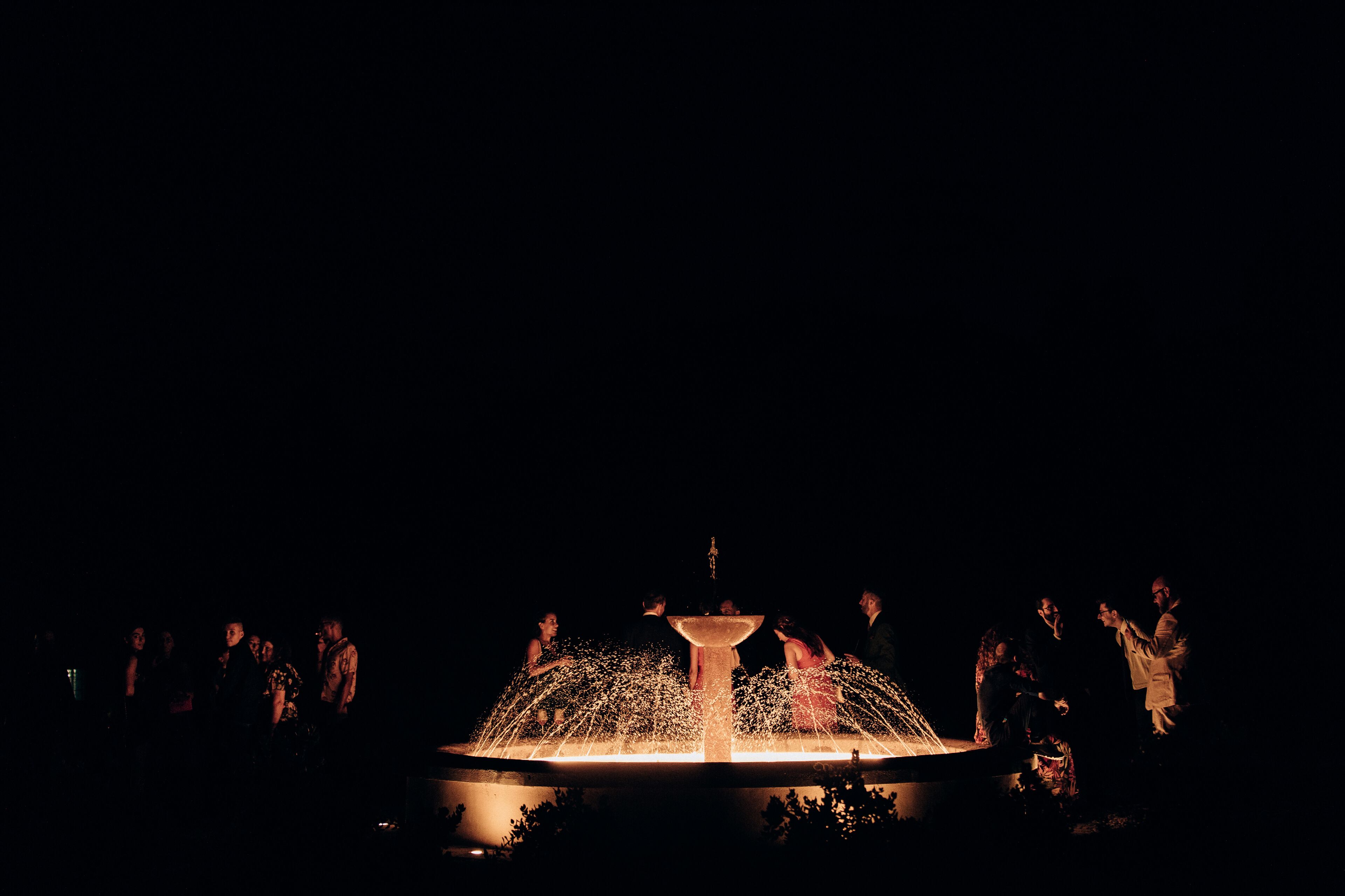 A fountain with water jets in a dark setting, surrounded by people.