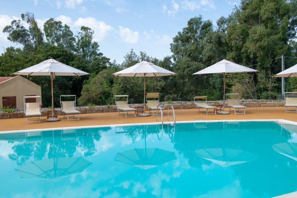 A swimming pool with lounge chairs and umbrellas, surrounded by trees.