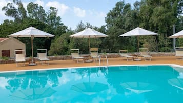A swimming pool with lounge chairs and umbrellas, surrounded by trees.