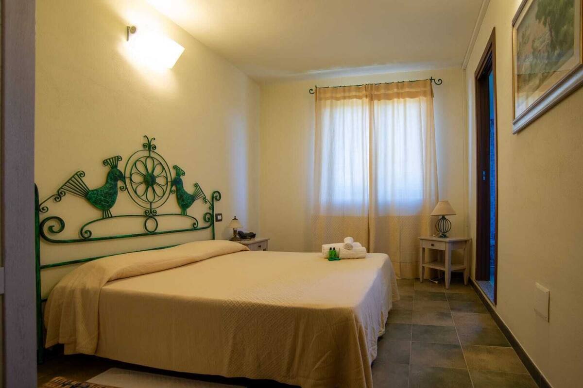 Una habitación de hotel con una cama, una mesita de noche, una lámpara y una ventana con cortinas.