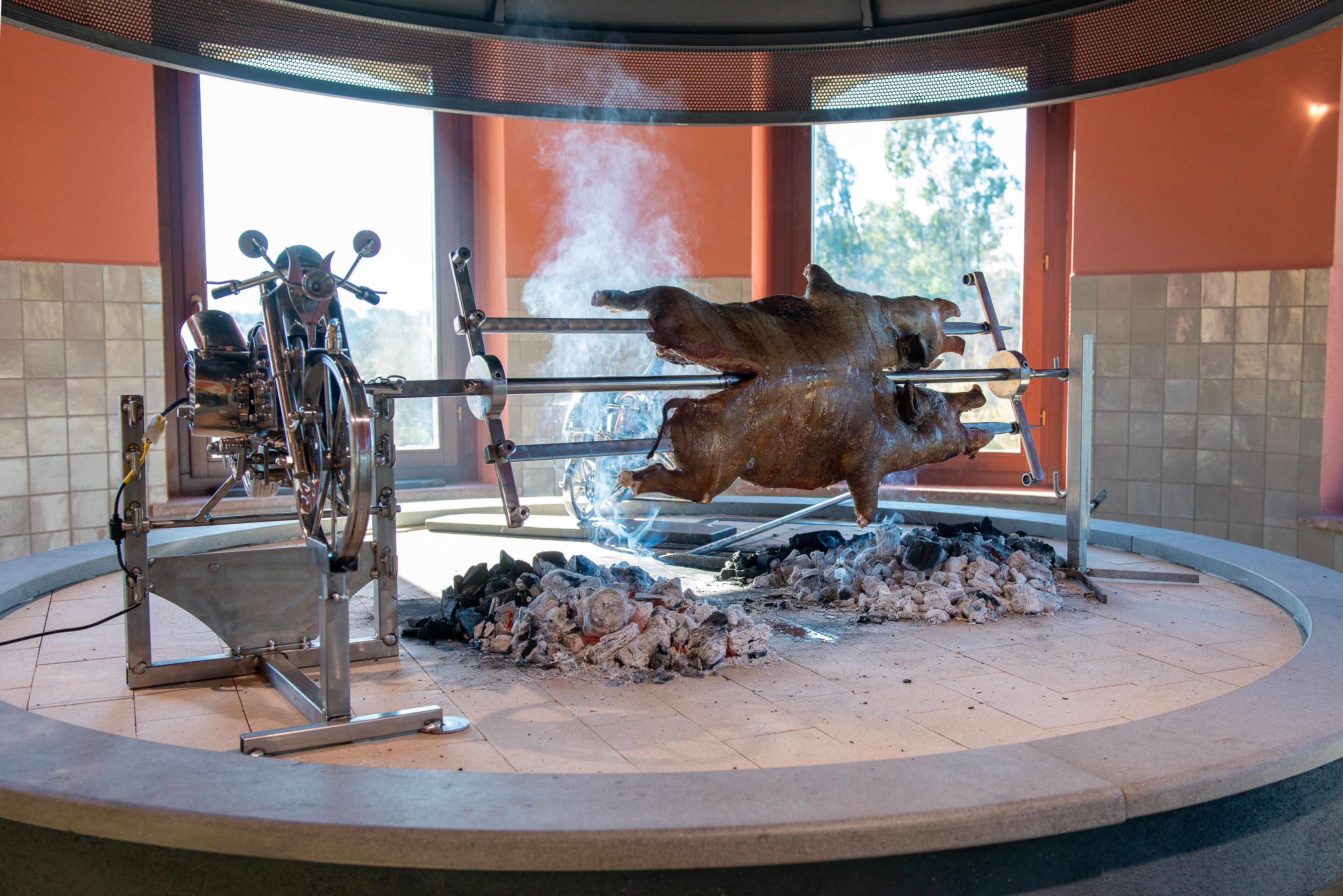 Un amplio espacio al aire libre para cocinar con un cerdo asado en trompo, una parrilla y un pozo para el fuego.
