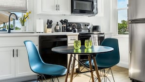 Une cuisine moderne avec des meubles blancs, un micro-ondes noir, un réfrigérateur en acier inoxydable et une table ronde entourée de chaises bleues.