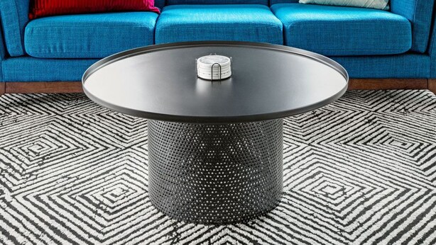 Un salon moderne avec un canapé bleu, une table basse ronde et un panneau lumineux néon sur lequel on peut lire « STL ».