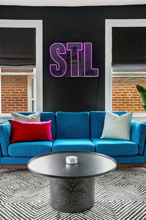 A modern living room with a blue sofa, a round coffee table, and a neon sign that reads "STL".