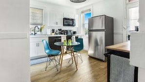 Une cuisine moderne avec des meubles blancs, un réfrigérateur en acier inoxydable, un four à micro-ondes et une table à manger avec des chaises bleues.