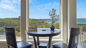 A room with a view of a lake and hills, a table with a vase of flowers, and two chairs. - Majestic View Getaway w/ Beautiful Lake Views! (Branson)