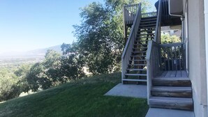 Eine Holztreppe führt zu einem Gebäude mit Blick auf ein Tal und Bäume.