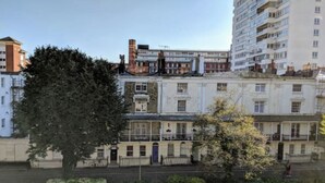 Un edificio de varios pisos con espacios residenciales y comerciales, destacando un árbol en primer plano.