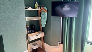 Una habitación con televisión montada en la pared, una estantería con tetera, cafetera y cubo de basura.