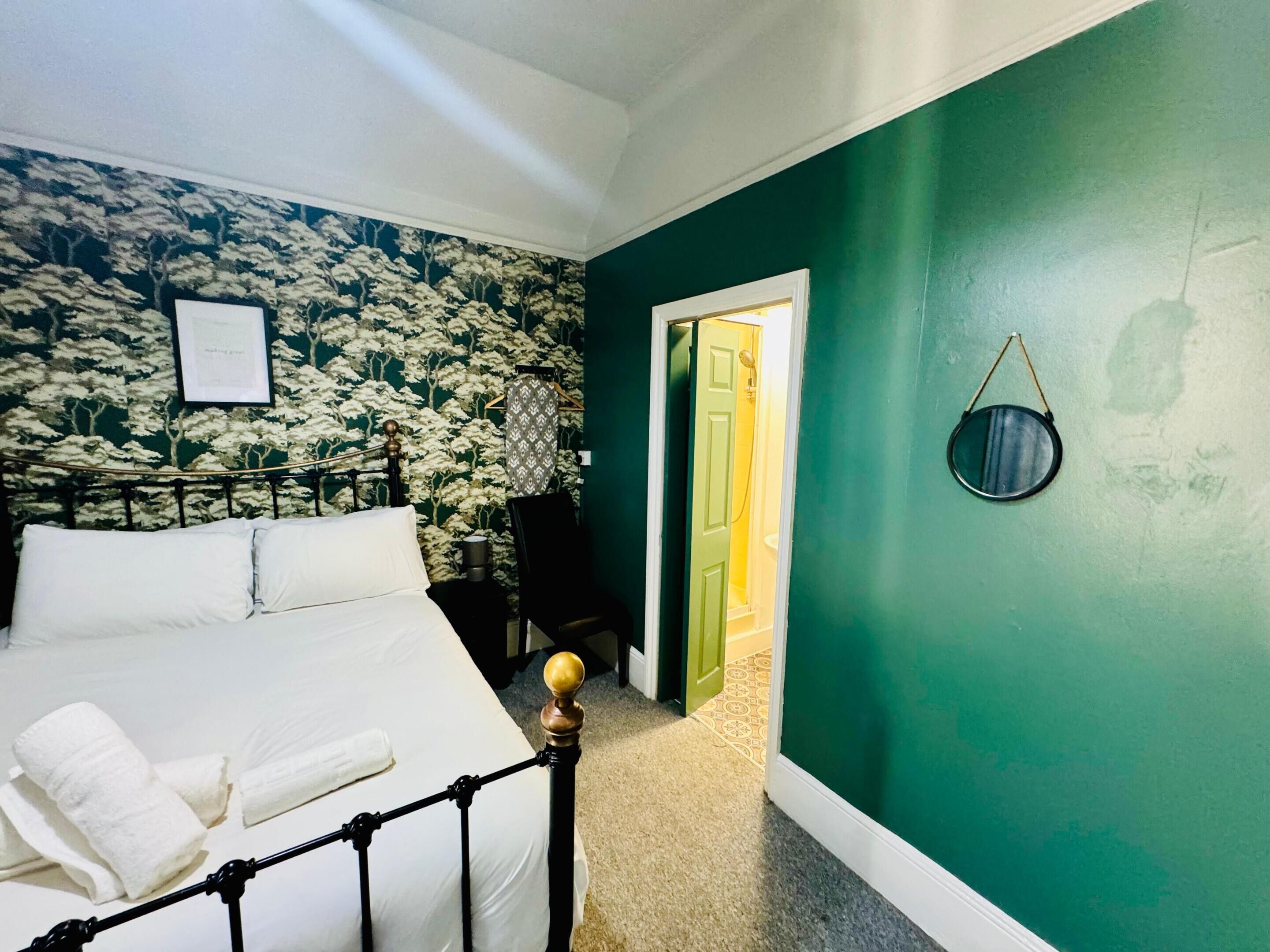 A bedroom with a bed, a green wall, a door leading to a bathroom, and a framed certificate on the wall.