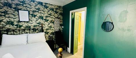 A bedroom with a bed, a green wall, a door leading to a bathroom, and a framed certificate on the wall.