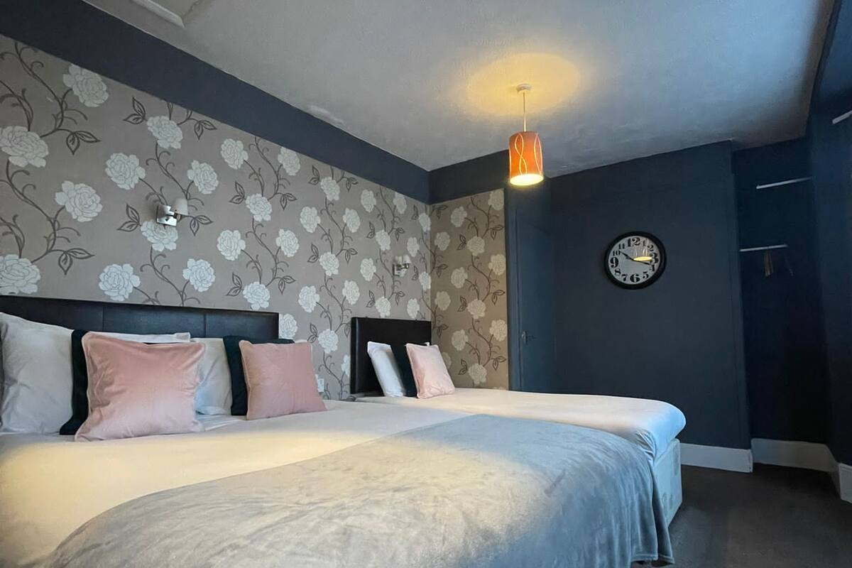 A hotel room with a large bed, two bedside tables, a wall clock, and a floral-patterned wallpaper.