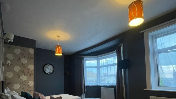 Un dormitorio con cama, un reloj, dos lámparas colgantes, un ventanal y un radiador.