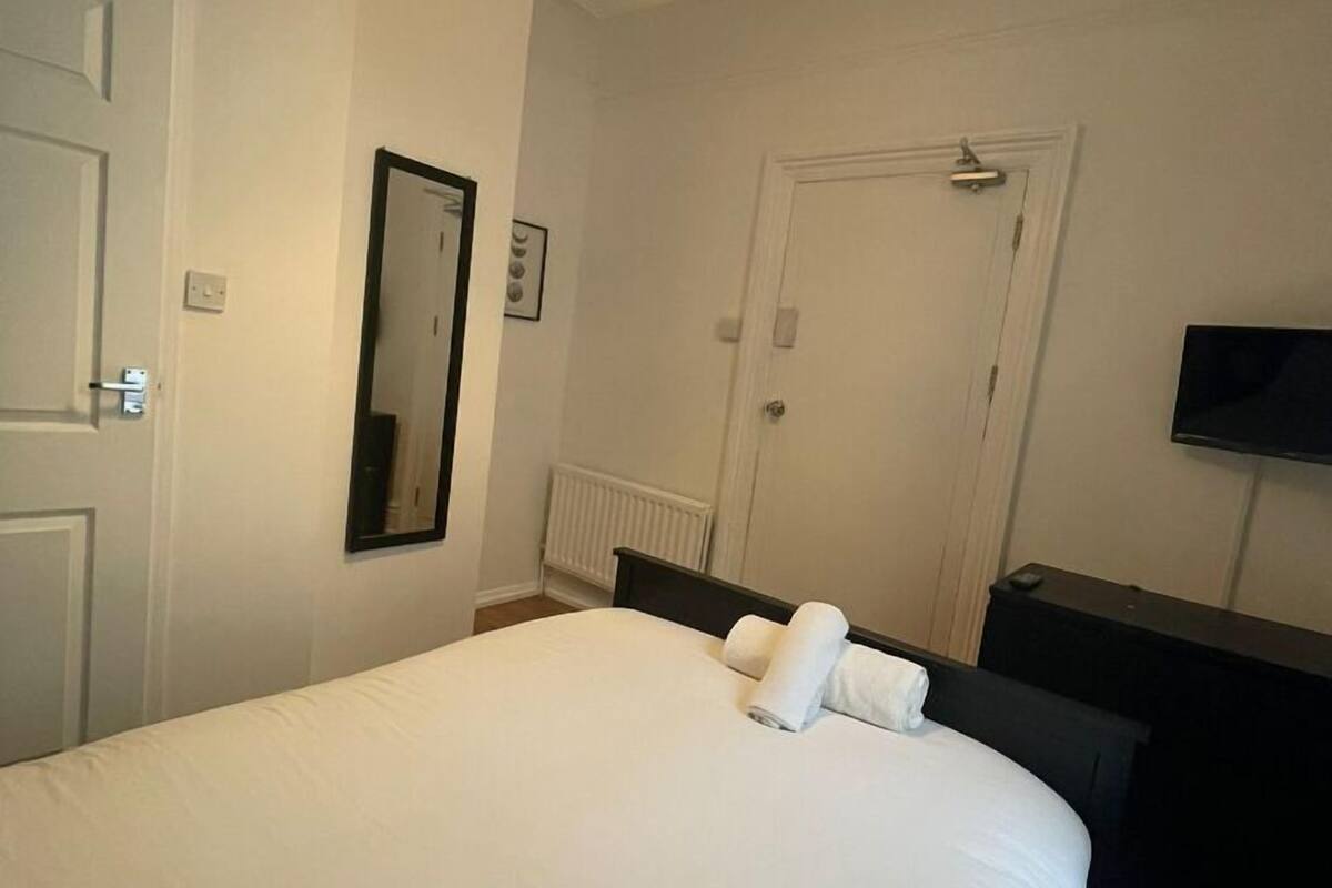 A hotel room with a large bed, a bedside table, a mirror, a radiator, and a television on the wall.