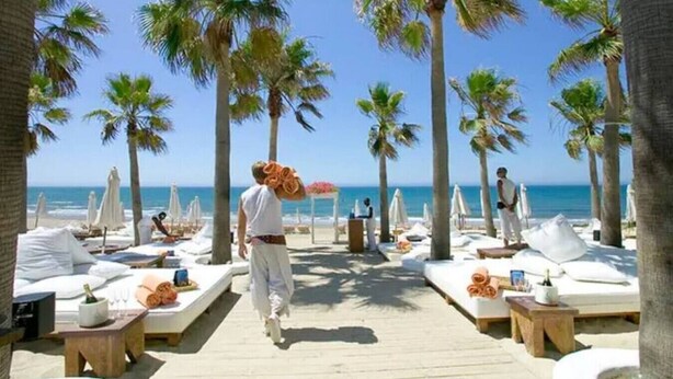 A beachside hotel with palm trees, sun loungers, and a wooden walkway. - Sun-lovers paradise,  all day sun and views. (Marbella)