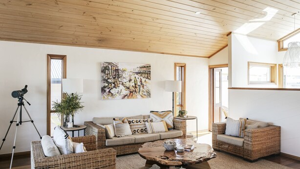 A spacious living room with a high ceiling, wicker furniture, a large painting, and a tripod.