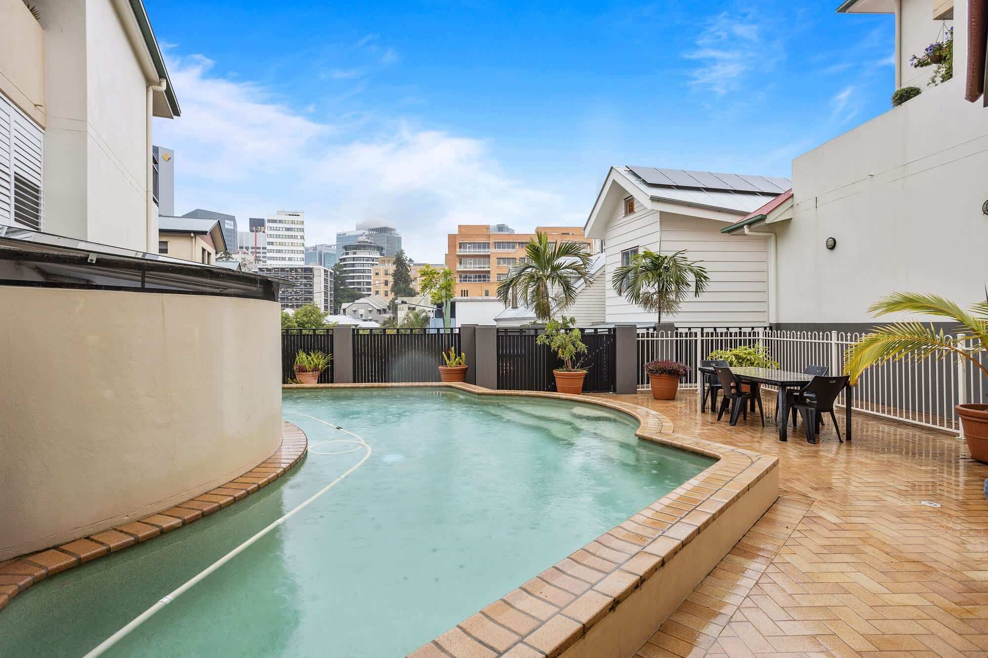 A swimming pool with a tiled deck, surrounded by potted plants and a white fence.