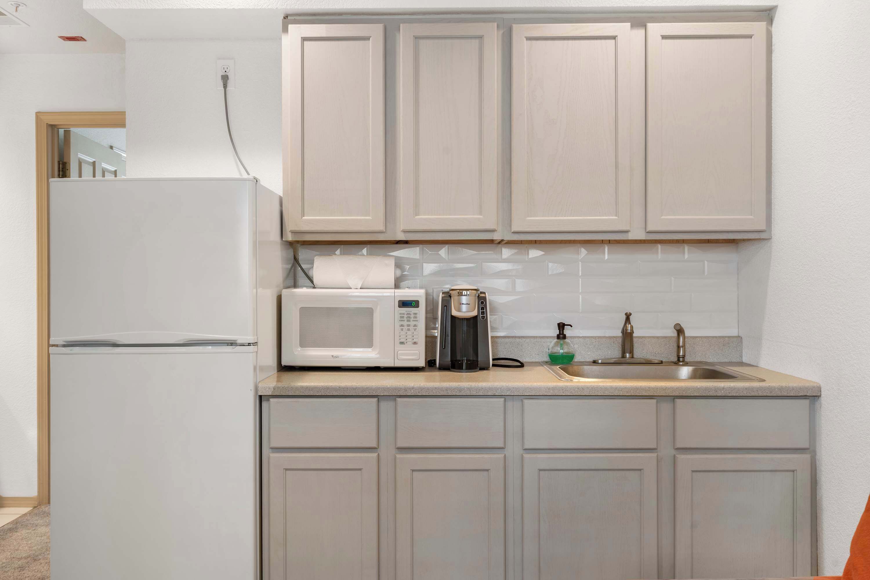 A compact kitchen with a refrigerator, microwave, coffee maker, and sink.