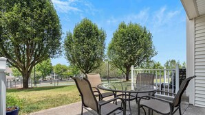 Une terrasse extérieure avec une table ronde et quatre chaises, entourée d’arbres et offrant une vue sur un parc.